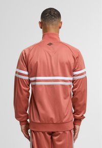 Rosa træningsjakke med høj krave, der har hvide striber over ryggen, ribbede manchetter og et logo-patch på nakken. Glat tekstur.