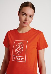Rode katoenen t-shirt met een ronde hals, korte mouwen, en een wit grafisch ontwerp met onderling verbonden vormen en de tekst "GGI2".