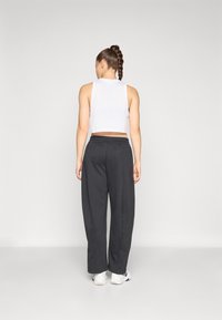 Bílý bezrukávový crop top, kombinovaný s voln�ými tmavě šedými tepláky s elastickým páskem. Model má na sobě bílé sportovní boty.