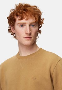 Huppari, jossa on ribbireunus kauluksessa ja hihansuissa. Edessä on pieni brodeerattu logo rinnassa. Suora pinta ja rento muotoilu.