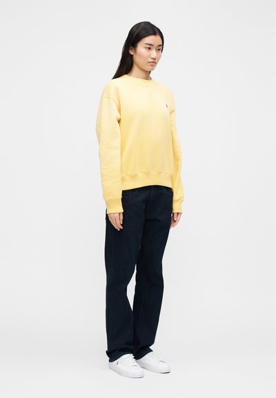Yellow sweatshirt with a round neckline and ribbed cuffs paired with dark blue jeans and white sneakers. Simple design, no patterns visible.