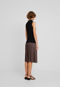 Schwarzes ärmelloses Oberteil mit Spitzen-Ausschnitt, kombiniert mit einem gemusterten braunen Rock mit fließendem Design, getragen mit schwarzen High Heels.