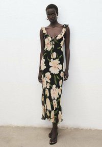 Zwarte bloemenjurk met een getailleerde silhoutte, ruches op de schouderbanden, roze bloemen en bladmotieven. Verfijnd met een strik bij de halslijn.