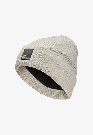 Gebreide beanie in lichtbeige met een omgeslagen rand en zwarte binnenkant. Heeft een rechthoekig zwart logo-opdruk aan de zijkant.