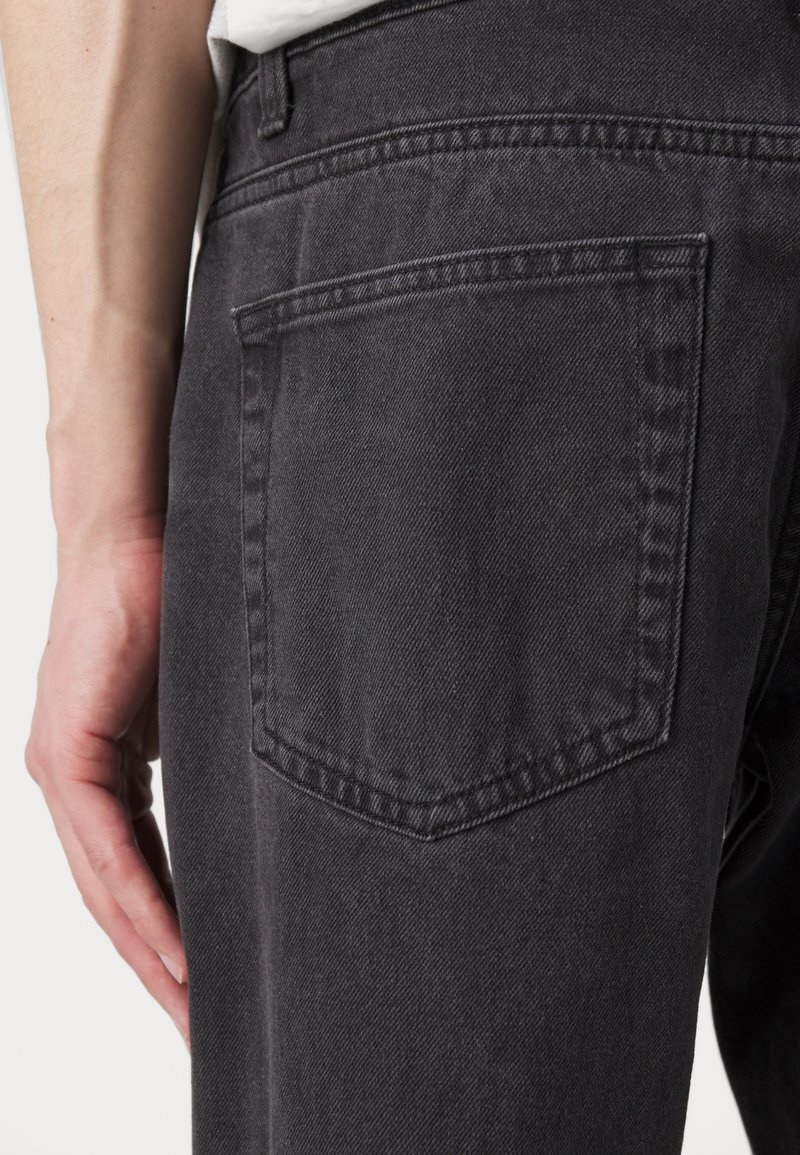 Schwarze Denim-Jeans mit strukturierter Oberfläche. Verfügt über eine Gesäßtasche, verstärkte Nähte und eine taillierte Passform entlang des Oberschenkels.