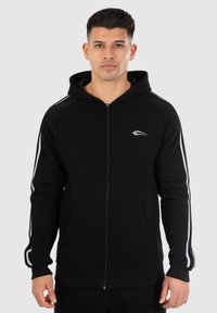 Felpa nera con zip e tasca frontale, righe grigie sulle maniche e logo bianco sul petto. Ha una vestibilità comoda e un cappuccio.