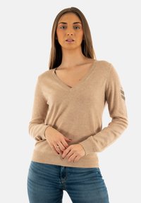 Pull beige en V en laine douce, à manches longues et avec des poignets côtelés ; il présente un design subtil sur la manche gauche.