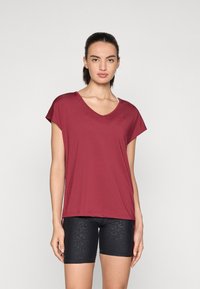 Bordeaux V-hals t-skjorte med korte ermer, kombinert med svarte teksturerte sykkelshorts. Stoffet ser glatt og elastisk ut.