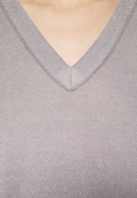 Gros plan sur un décolleté avec un haut en V violet clair pailleté sur une peau claire.