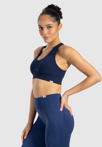 Marinblå ribbat sportbh med breda axelband, kombinerad med högmidjade leggings. Båda plaggen har en slät yta och minimal varumärkeslogga.