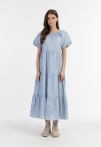 Jasnoniebieska, paskowana sukienka maxi z krótkimi bufkami, zebranym w pasie oraz warstwową spódnicą. Noszona z beżowymi, lace-up botkami.