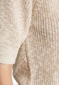 Jersey de punto beige con un patrón texturizado, con costura suelta y puños enrollados. Tejido suave con un corte relajado.