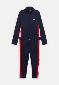 Granatowy dres Adidas z pełnym zamkiem z przodu, czerwono-białe paski po bokach kurtki i spodni oraz logo Adidas na piersi.