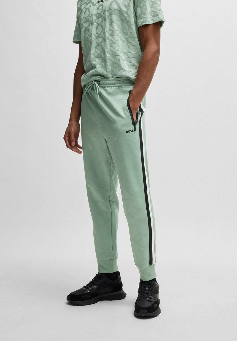 Ljusgröna joggingbyxor med ett texturerat mönster, svarta sidostråkar, elastisk midja och fickor, i kombination med en matchande t-shirt med textur.