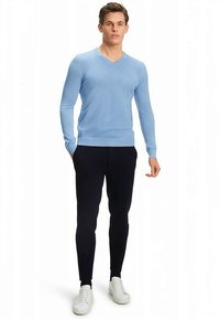 Hellblauer V-Ausschnitt-Pullover aus glattem Stoff, kombiniert mit dunkel sitzender Slim-Fit-Hose und weißen Sneakers. Einfaches, modernes Design.