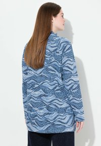 Maglietta a manica lunga blu con un motivo ondulato in varie sfumature di blu e nero. Tessuto morbido con una vestibilità comoda e scollo alto.
