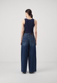 Tamna plava majica bez rukava uparena s širokim, izblijedjelim plavim trapericama s četiri džepa i strganim rubovima. Minimalistički dizajn.