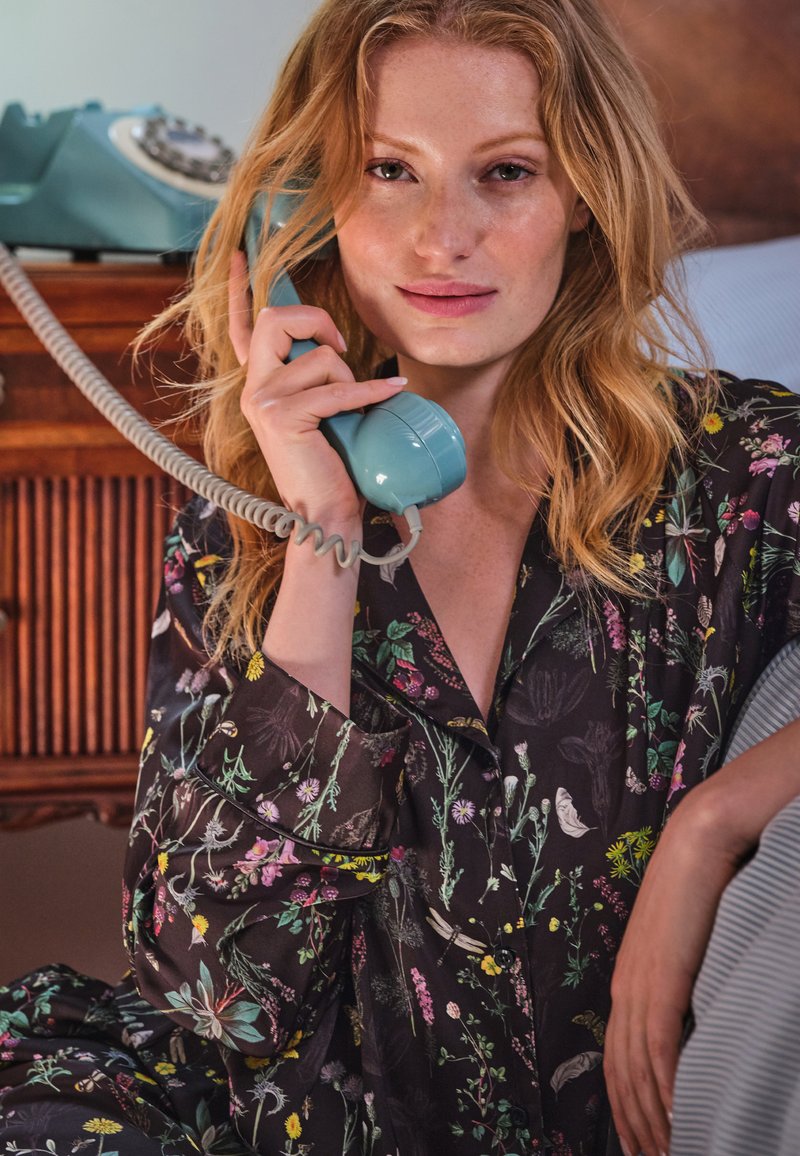 Colorful floral-patterned pajama set on a figure. The figure holds a retro turquoise rotary phone with a coiled cord against a wooden background.