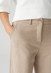 Beige textuur broek met een rechte snit, zijzakken en een enkele knoopsluiting bij de tailleband, gecombineerd met een witte top.