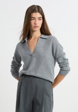 Pullover grigio strutturato con design a V e colletto, maniche lunghe, abbinato a pantaloni grigi su misura.