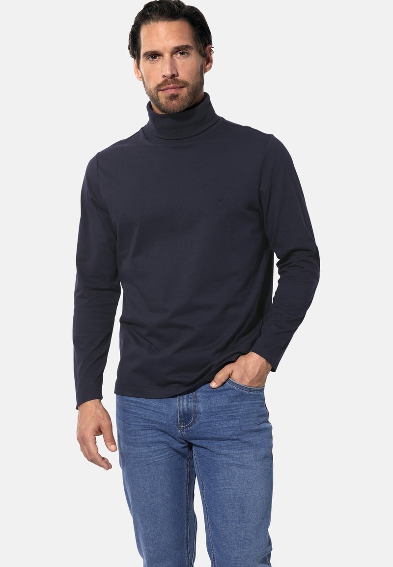 Marinefarbene Rollkragenshirt aus weichem Stoff, mit langen Ärmeln und einem dezenten Logo. Kombiniert mit blauen Jeans, die eine taillierte Silhouette zeigen.