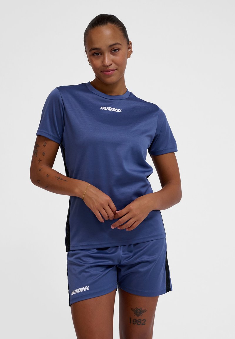 Camiseta deportiva de manga corta azul y pantalones cortos a juego con acentos laterales negros. Presenta el logo "HUMMEL" en blanco en ambas piezas. Tejido suave y transpirable.