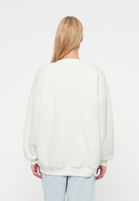 Hvit, lodden genser med oversized silhuett, senkede skuldre og ribbede mansjetter. Jevn tekstur, uformelt design og rund hals.