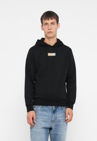 Felpa nera con cappuccio, tasca a marsupio, cordino regolabile e un piccolo logo bianco e arancione sul petto. Tessuto morbido in misto cotone.