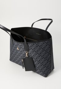 Black tote bag featuring a geometric pattern, leather material, two handles, an interior zip pocket, and an attached black card holder.