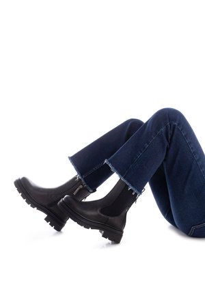 Botines de cuero negro con paneles laterales elásticos, suelas de goma gruesa y cremalleras laterales, combinados con unos pantalones de mezclilla de tiro alto de campana de color azul oscuro con dobladillos deshilachados.