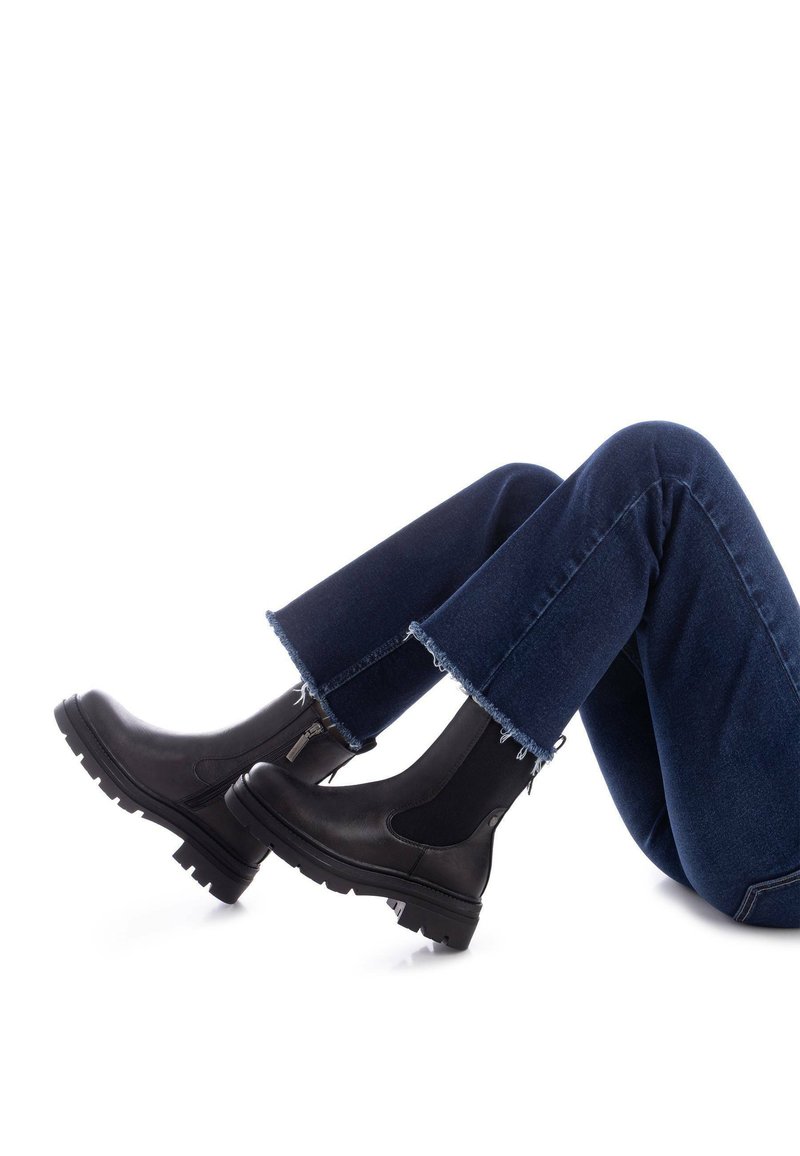 Stivali ankle in pelle nera con pannelli elastici laterali, suole in gomma spesse e cerniere laterali, abbinati a jeans a zampa d'elefante in denim blu scuro con orli sfrangiati.