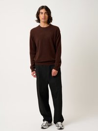 Maglione lavorato a maglia marrone, vestibilità rilassata, polsini a costine; pantaloni neri a gamba larga; sneakers bianche e grigie testurizzate. Stile minimalista, palette neutra.