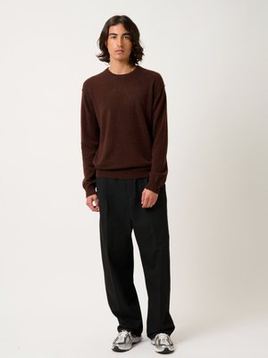 Bruine gebreide trui, losse pasvorm, geribde manchetten; zwarte wijde broek; gestructureerde witte en grijze sneakers. Minimalistische stijl, neutrale kleurenpalet.