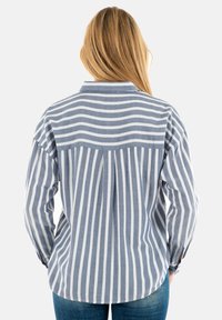 Camisa de rayas azul y blanca con cuello, mangas largas y dobladillo ligeramente curvado. Tejido texturizado con rayas verticales.