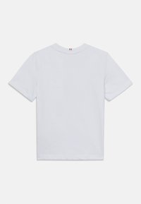 T-shirt en coton blanc à manches courtes et col rond, avec un petit détail brodé rouge, blanc et bleu au niveau de l'encolure arrière.