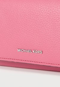 Ροζ δερμάτινο πορτοφόλι με υφή στην επιφάνεια και ανάγλυφο λογότυπο "MICHAEL KORS" σε ασημί. Ραφές κατά μήκος των ακμών.
