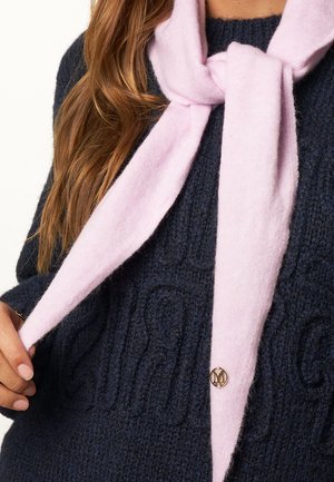 Light pink scarf made of soft fabric, tied around the neck, layered over a dark navy textured sweater with a small gold accent detail.