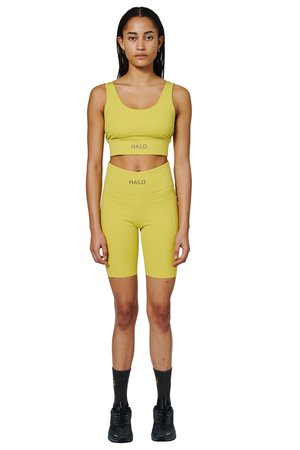 Kvinde, der står frontal med gul cropped top og matchende højtaljede cykelshorts med sorte sokker og sko.