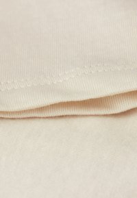Tessuto beige chiaro con una consistenza liscia, caratterizzato da un bordo cucito e una caduta morbida. Sono visibili due strati, che mostrano pieghe distintive.
