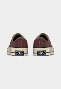 Ζευγάρι μαρονιέ χαμηλά παπούτσια Converse All Star, εμφανιζόμενα από πίσω, με λευκές λαστιχένιες σόλες και μαύρα λογότυπα.