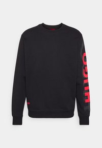 Svart sweatshirt med rund halsringning, ribbad mudd och nederkant. Har ett iögonfallande rött "HUGO"-tryckdesign på vänster ärm och en liten röd logotyp längst ner.