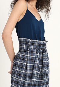 Tummansininen spagettihihnallinen toppi, joka on yhdistetty korkeavyötäröiseen ruutuhameeseen, jossa on sinivalkoisia ruutuja ja edessä solmittava rusetti.