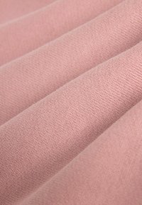 Tissu rose doux et plié, montrant une texture fine en tricot avec des motifs de couture visibles et des ombres douces mettant en valeur les plis.