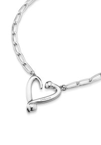 Pendentif en argent en forme de cœur sur une chaîne, présentant des courbes lisses et une finition polie. La chaîne possède des maillons allongés avec une texture brillante.