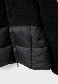 Črn flis jakna s teksturirano, puhasto zgornjo stranjo in gladkim, podloženim spodnjim delom. Vključuje zadrgo na strani.