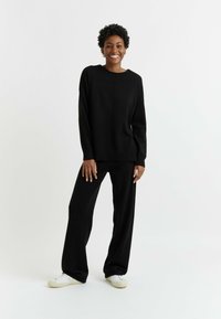 Maglione nero a maglia con una vestibilità comoda, maniche lunghe e dettagli a coste abbinato a pantaloni neri a gamba larga. Le sneakers sono bianche con dettagli testurizzati.