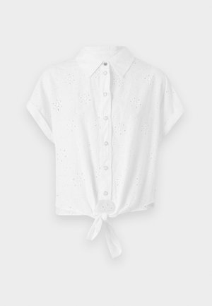 Bijela košulja kratkih rukava s ovratnikom, prednjim gumbima i čvorom na donjem rubu. Sadrži izvezenu oblikovanu mrežu za teksturu i detalje.