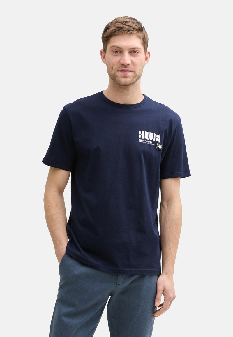 Námořnická modrá bavlněná tričko s krátkými rukávy a kulatým výstřihem. Má potisk na hrudi s texty "BLUE" a "TOM TAILOR" v bílé barvě.