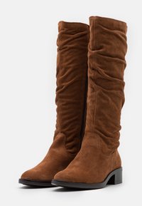 Bottes montantes en daim marron avec un design froissé, dotées d'une fermeture éclair latérale et d'un petit talon bloc. Texture douce sans motifs visibles.