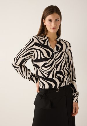Black and white zebra print blouse with buttons, long sleeves, and a collar, paired with a black skirt featuring a belt and layered design.